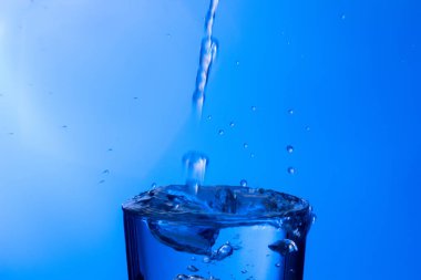 Temiz, içme suyu temiz bir bardağa dökülüyor, sağlıklı, sağlıklı, temiz, kokusuz ve tatsız bir su. Yüzeye su damlaları sıçrıyor. Jet su bardağa giriyor