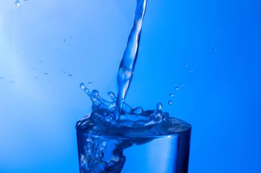 Temiz, içme suyu temiz bir bardağa dökülüyor, sağlıklı, sağlıklı, temiz, kokusuz ve tatsız bir su. Yüzeye su damlaları sıçrıyor. Jet su bardağa giriyor