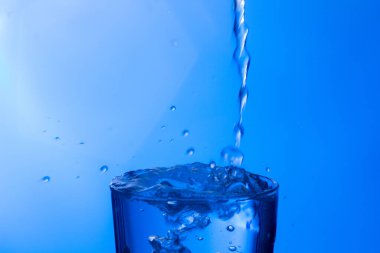 Temiz, içme suyu temiz bir bardağa dökülüyor, sağlıklı, sağlıklı, temiz, kokusuz ve tatsız bir su. Yüzeye su damlaları sıçrıyor. Jet su bardağa giriyor