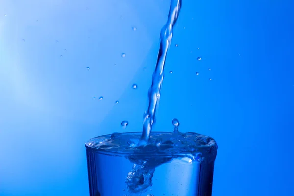 Temiz, içme suyu temiz bir bardağa dökülüyor, sağlıklı, sağlıklı, temiz, kokusuz ve tatsız bir su. Yüzeye su damlaları sıçrıyor. Jet su bardağa giriyor