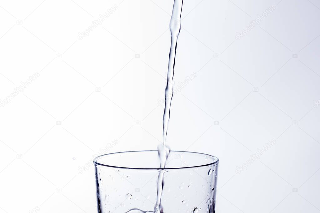 Clear, drinking water falls into a clear glass, healthy, wholesome, fresh water with no odor or taste. Splash of water drops splashing onto the surface. Jet of water entering the glass