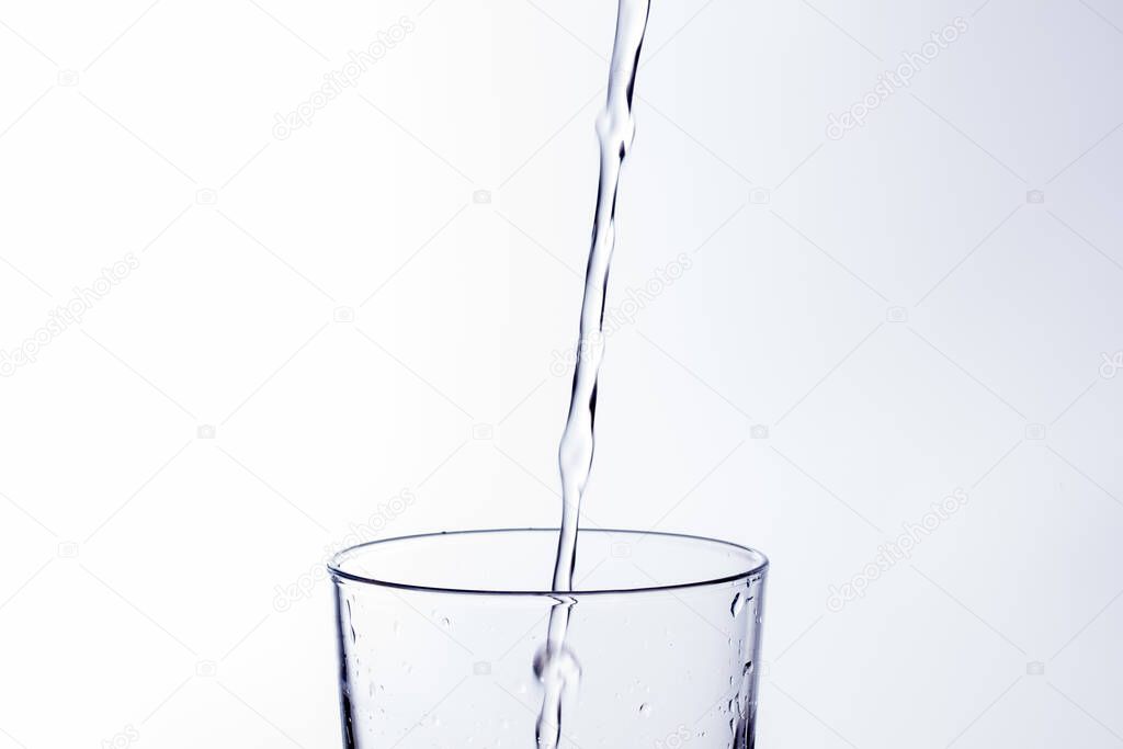Clear, drinking water falls into a clear glass, healthy, wholesome, fresh water with no odor or taste. Splash of water drops splashing onto the surface. Jet of water entering the glass