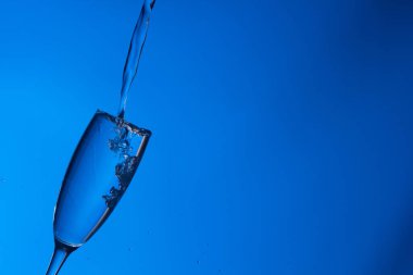 Temiz, içme suyu temiz bir bardağa dökülüyor, sağlıklı, sağlıklı, temiz, kokusuz ve tatsız bir su. Yüzeye su damlaları sıçrıyor. Jet su bardağa giriyor