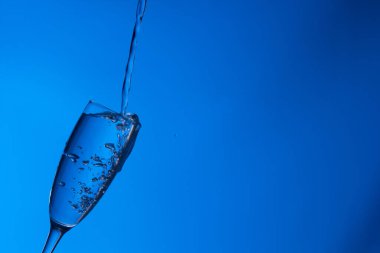 Temiz, içme suyu temiz bir bardağa dökülüyor, sağlıklı, sağlıklı, temiz, kokusuz ve tatsız bir su. Yüzeye su damlaları sıçrıyor. Jet su bardağa giriyor