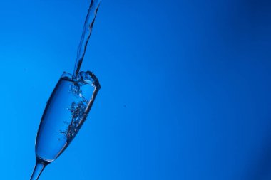 Temiz, içme suyu temiz bir bardağa dökülüyor, sağlıklı, sağlıklı, temiz, kokusuz ve tatsız bir su. Yüzeye su damlaları sıçrıyor. Jet su bardağa giriyor