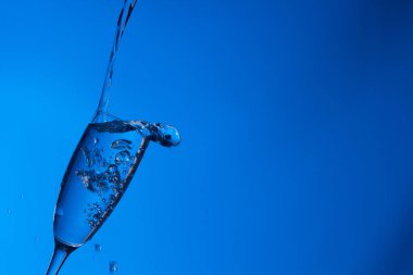 Temiz, içme suyu temiz bir bardağa dökülüyor, sağlıklı, sağlıklı, temiz, kokusuz ve tatsız bir su. Yüzeye su damlaları sıçrıyor. Jet su bardağa giriyor