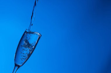 Temiz, içme suyu temiz bir bardağa dökülüyor, sağlıklı, sağlıklı, temiz, kokusuz ve tatsız bir su. Yüzeye su damlaları sıçrıyor. Jet su bardağa giriyor