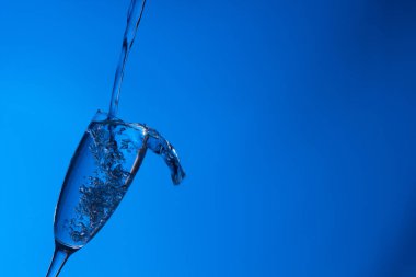 Temiz, içme suyu temiz bir bardağa dökülüyor, sağlıklı, sağlıklı, temiz, kokusuz ve tatsız bir su. Yüzeye su damlaları sıçrıyor. Jet su bardağa giriyor