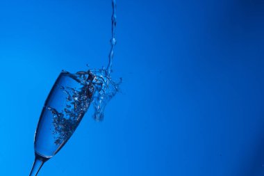 Temiz, içme suyu temiz bir bardağa dökülüyor, sağlıklı, sağlıklı, temiz, kokusuz ve tatsız bir su. Yüzeye su damlaları sıçrıyor. Jet su bardağa giriyor