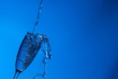 Temiz, içme suyu temiz bir bardağa dökülüyor, sağlıklı, sağlıklı, temiz, kokusuz ve tatsız bir su. Yüzeye su damlaları sıçrıyor. Jet su bardağa giriyor