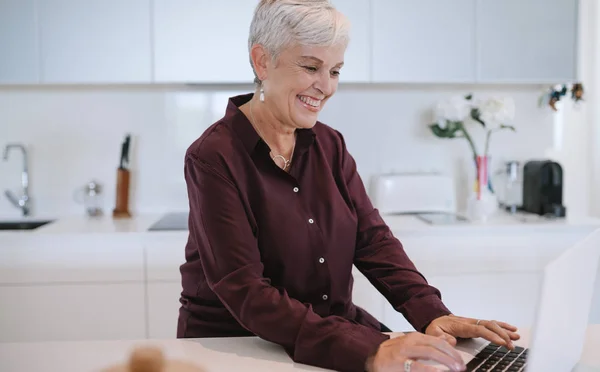 Portrait of a beautiful mature woman smiling, typing on her laptop