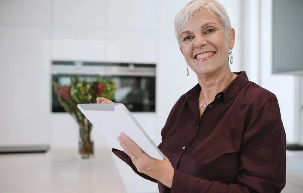 Portrait of a mature woman smiling, using her tablet at home