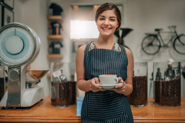 Young beautiful waitress smiling serving coffee with latte art