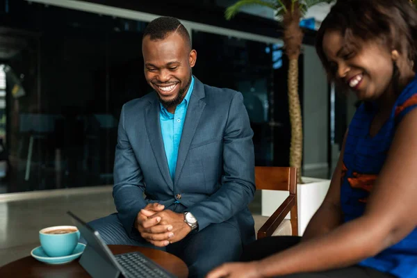 两名笑着的年轻非洲商人在一个办公室边喝咖啡边在一块数字平板电脑上一起工作 — 图库照片