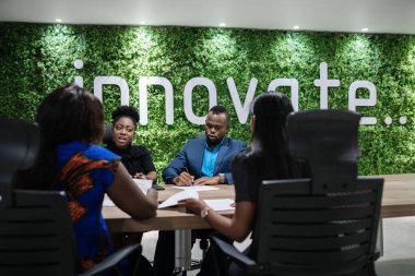 Genç Afrikalı iş kadını, bir ofis masasındaki toplantı sırasında bir grup meslektaşıyla iş görüşmesi yapıyor.