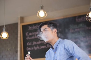 Mavi tişört giyen genç Asyalı adam, tütün ya da sigara dumanıyla nefes ver.