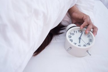Adam beyaz yatakta beyaz alarm saati ile sabah uyku.