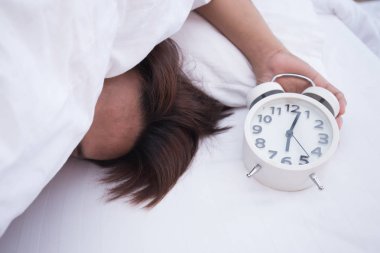 Adam beyaz yatakta beyaz alarm saati ile sabah uyku.