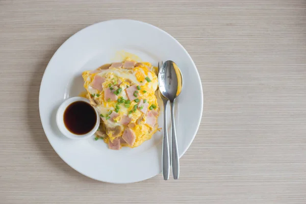 Omelette with pork cut bacon on rice and sauce on white ceramic plate and spoon and fork