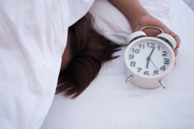Adam beyaz yatakta beyaz alarm saati ile sabah uyku.