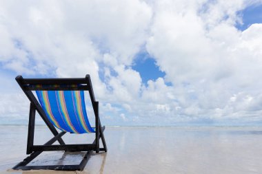 Mavi ahşap plaj sandalyesi beyaz bulutlar ve yaz sezonu gelince mavi gökyüzü ile sahilde