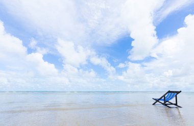 Mavi ahşap plaj sandalyesi beyaz bulutlar ve yaz sezonu gelince mavi gökyüzü ile sahilde