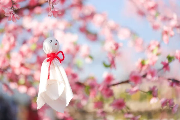 Yağmur bebeği, beyaz bez bebek pembe çiçek ağacı ya da Sakura 'nın altına asılmış. Teru teru bouzu Japonca yağmur önleyici bebek anlamına gelir.