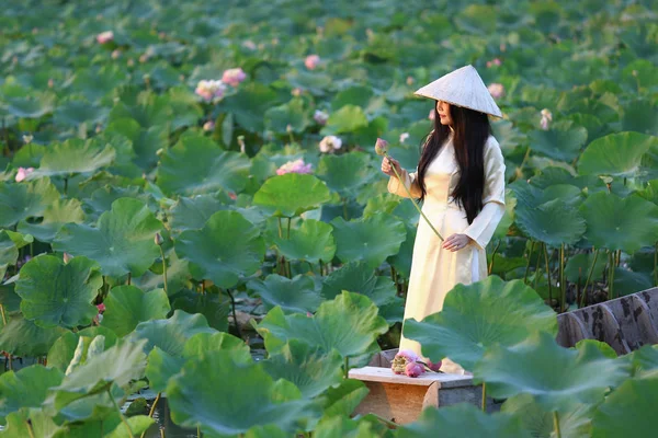 Ahşap antik tekne ile lotus gölet ao dai traditonal vietnamlı sarı ve beyaz elbise Vietnamlı kadın.