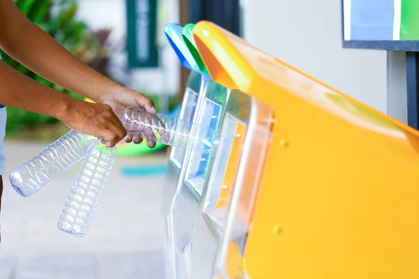 Erkek eli boş plastik şişe yeşil dünya için çevre ve geri dönüşüm fikir olarak yeşil çöp kutusu koyarak.
