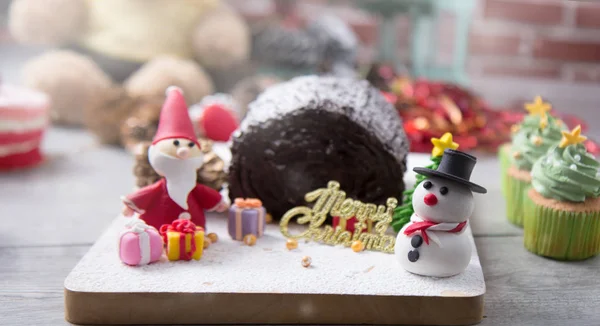 Log cake with assorted sugar paste, Santa Claus, Snow man with hat, pine tree and Merry Christmas sign on wood cutter for celebrating Joyeaux Noel