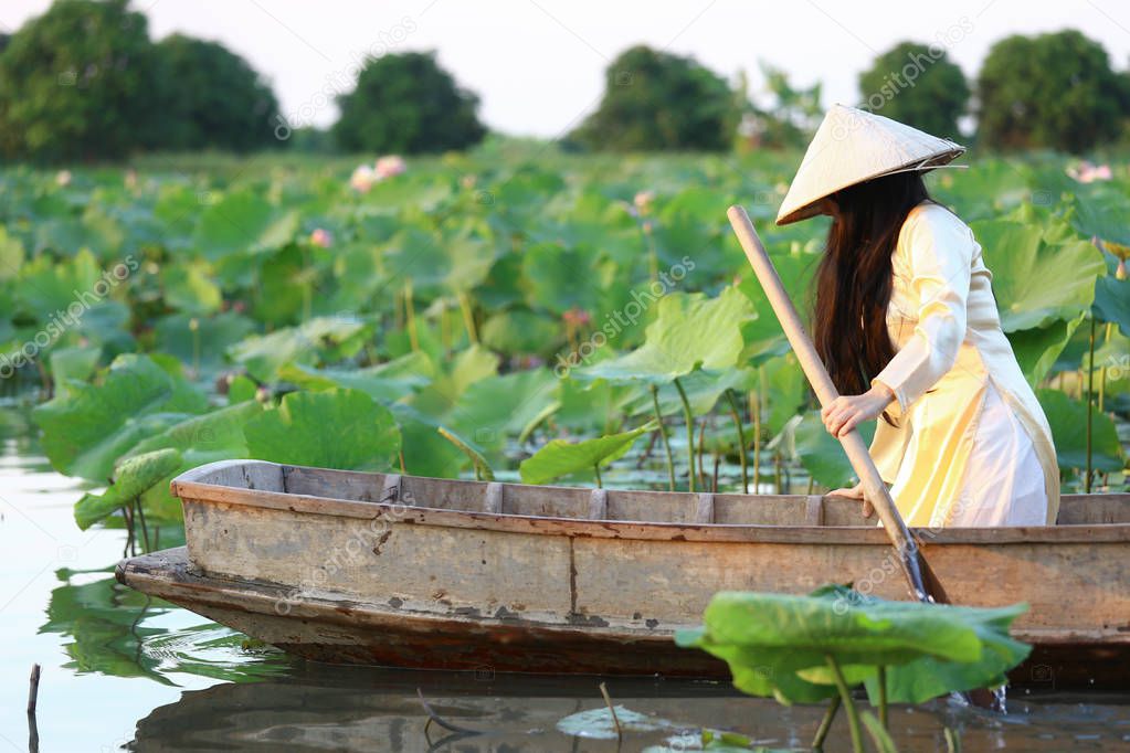 Vietnamese woman in ao dai traditional vietnamese yellow and white  dress in lotus pond with wood ancient boat.