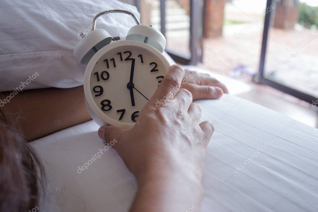 Man sleeping on white bed with white alarm clock in morning
