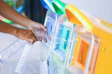 Erkek eli boş plastik şişe yeşil dünya için çevre ve geri dönüşüm fikir olarak yeşil çöp kutusu koyarak.