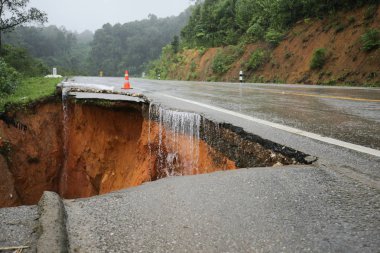 Şiddetli yağmurların yol açtığı heyelan, bozuk yol asfaltına neden olur. Sokakta yıkılmış çimento. Toprak kaymasından çıkan çatlak yol sağanak yağış yüzünden mahvoldu.
