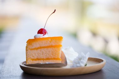 Kırmızı kirazlı, çırpılmış kremalı ve tahta tabakta beyaz çiçekli turuncu pasta. Tatlı ve ekşi tatlı..