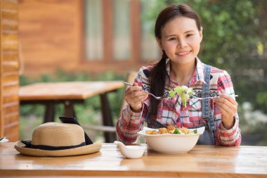 Asyalı kadın sağlıklı salatasının tadını çıkarıyor. Bahçedeki büyük beyaz kasede kıtır kıtır salata yiyor.