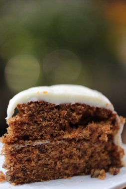 Çelik kaşıkla beyaz seramik tabakta kremalı beyaz çikolatalı havuçlu kek.