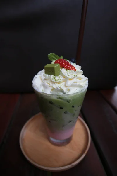 Cold beverage, green tea smoothie with strawberry and blueberry and creamy on top with plastic straw in tall glass