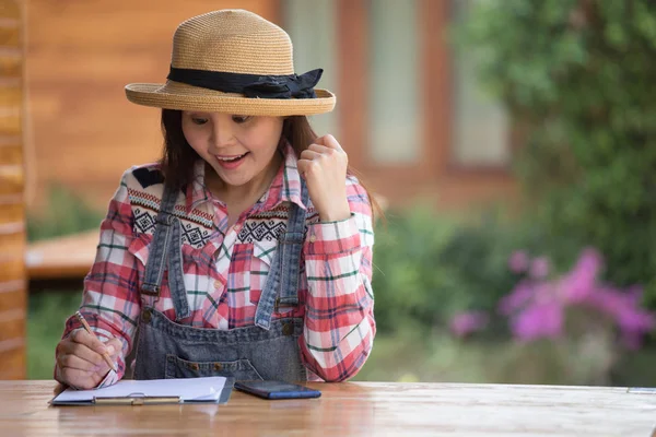 Asian beautiful country woman in farm worker shirt sitting and writing on paper outside in the garden