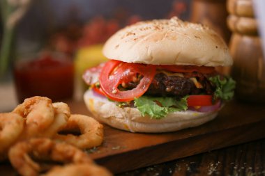 Koyu tonda sığır burger, ahşap tabakta loş ışık ve arka planda koyu renk