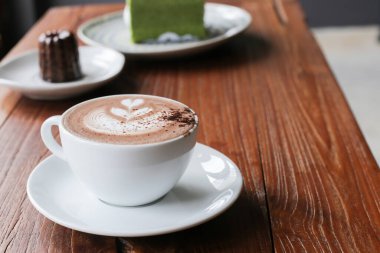 Kahve dükkanındaki ahşap sehpanın üzerindeki beyaz seramik bardağın üstünde lale sütlü sütlü kahve.