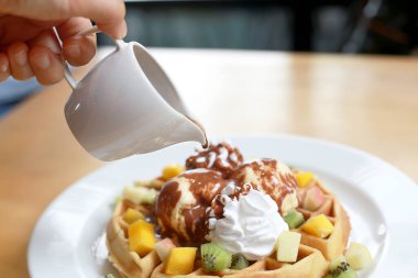 Dondurmalı çikolatalı waffle ve çırpılmış krema ve üstten küçük kavanozlarla sulanan çikolatalı top domuz. Beyaz tabakta tatlı soğuk Avrupa tatlısı.