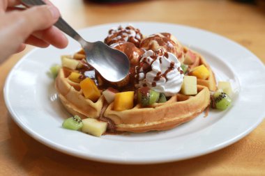 Dondurmalı çikolatalı waffle ve çırpılmış krema ve üstten küçük kavanozlarla sulanan çikolatalı top domuz. Beyaz tabakta tatlı soğuk Avrupa tatlısı.