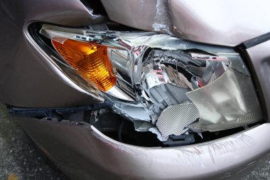 Altın rengi kahverengi arabanın ön lambası kırılmış. Çarpışan araba parçalanmış. Araba kazası sigortası önemlidir.