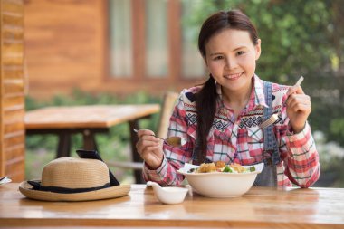 Asyalı kadın sağlıklı salatasının tadını çıkarıyor. Bahçedeki büyük beyaz kasede kıtır kıtır salata yiyor.