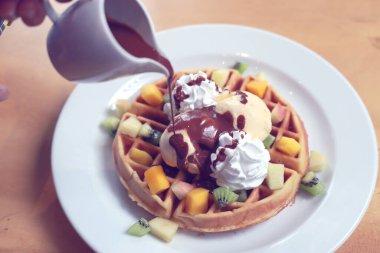 Dondurmalı çikolatalı waffle ve çırpılmış krema ve üstten küçük kavanozlarla sulanan çikolatalı top domuz. Beyaz tabakta tatlı soğuk Avrupa tatlısı.