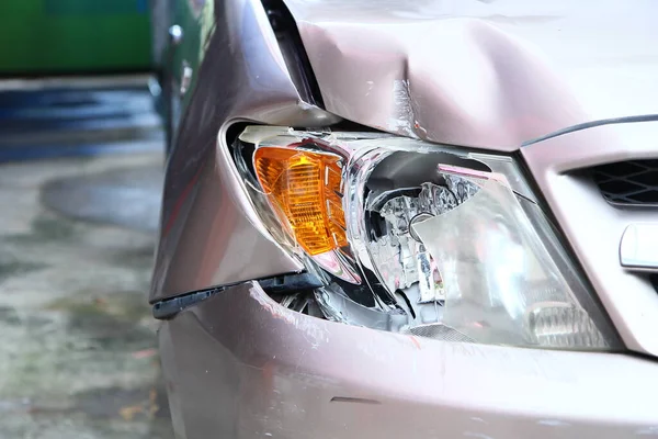 Altın rengi kahverengi arabanın ön lambası kırılmış. Çarpışan araba parçalanmış. Araba kazası sigortası önemlidir.