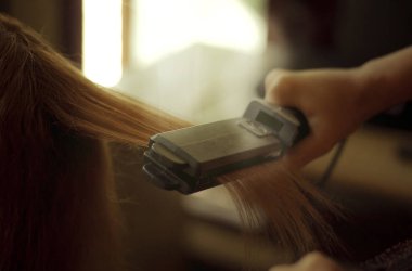 Güzellik uzmanı müşteri için saç düzleştirici kullanıyor.