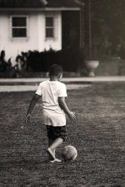 Kırsal kesimdeki çocuklar sahada futbol uyguluyorlar, futbol topları yerine voleybol topları kullanıyorlar, siyah-beyaz.