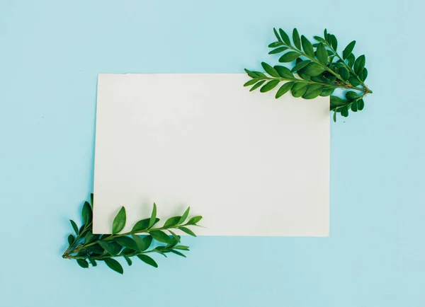 Desktop mock-up with blank paper card, branch on white shabby table background. Empty space. Styled stock photo, web banner. Flat lay, top view.